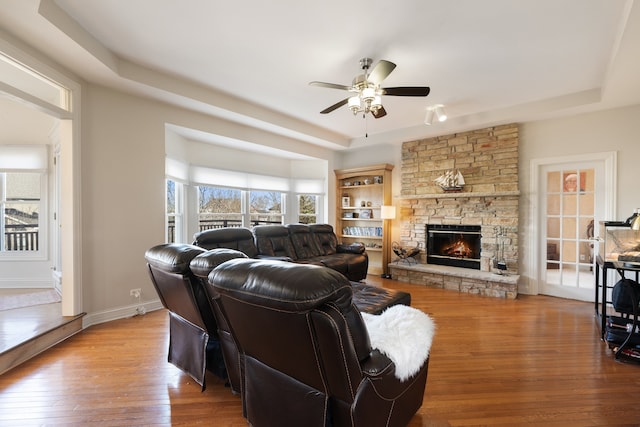 living room featuring hardwood / wood-style floors, baseboards, a tray ceiling, a fireplace, and ceiling fan