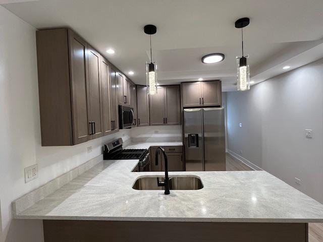 kitchen featuring hanging light fixtures, a peninsula, appliances with stainless steel finishes, and a sink