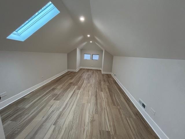 additional living space with visible vents, baseboards, wood finished floors, and lofted ceiling with skylight