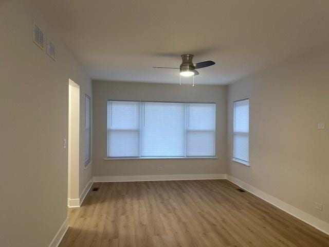 empty room with a ceiling fan, wood finished floors, baseboards, visible vents, and a wealth of natural light