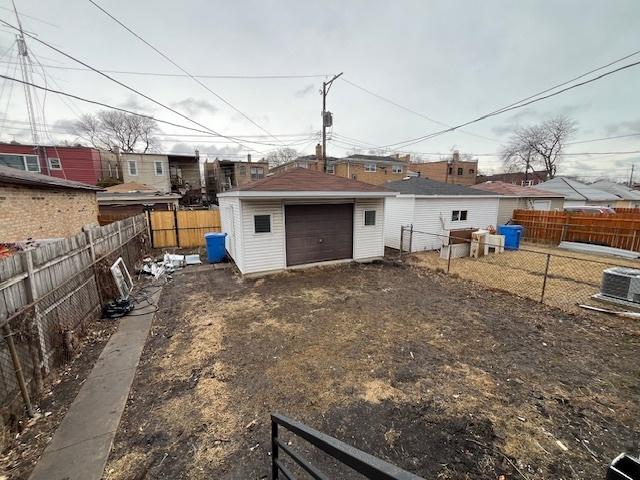 back of property with an outbuilding, driveway, a detached garage, central AC, and a fenced backyard