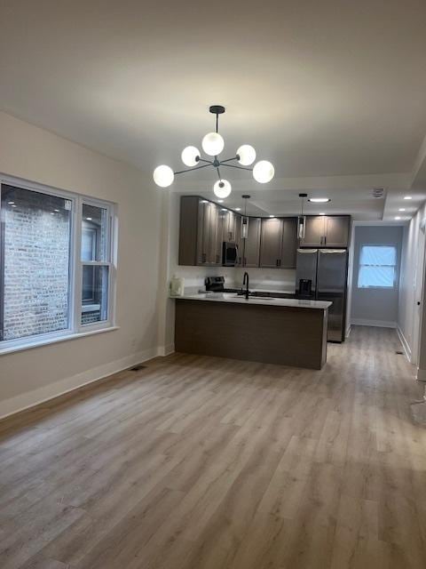 kitchen featuring refrigerator with ice dispenser, stainless steel microwave, a peninsula, light wood finished floors, and baseboards