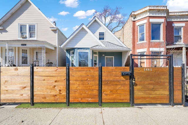 view of front facade with a gate, a fenced front yard, and roof with shingles