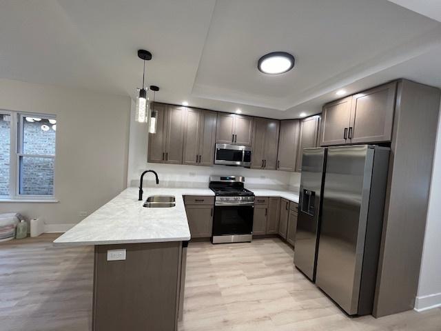 kitchen with appliances with stainless steel finishes, light countertops, a sink, a peninsula, and a tray ceiling