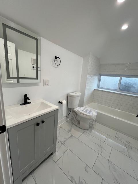 bathroom with vaulted ceiling, marble finish floor, a tub to relax in, toilet, and vanity