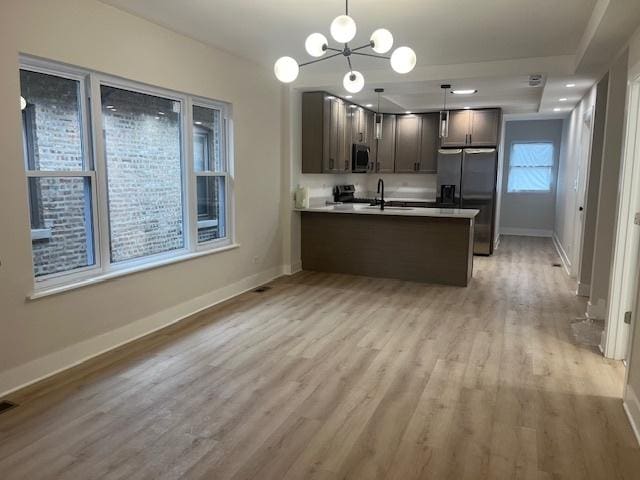 kitchen featuring an inviting chandelier, a sink, stainless steel appliances, light wood-style flooring, and a peninsula