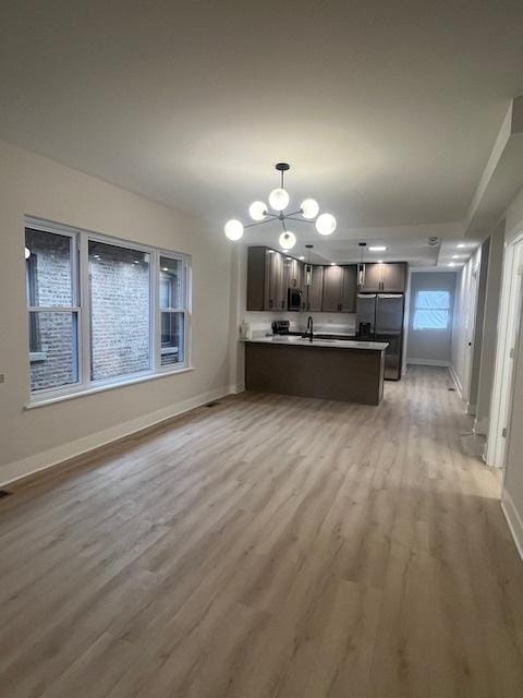 kitchen featuring light wood finished floors, an inviting chandelier, a peninsula, baseboards, and appliances with stainless steel finishes