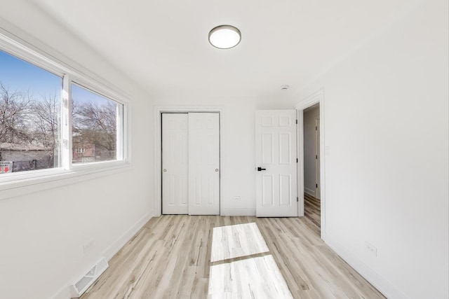 unfurnished bedroom featuring a closet, visible vents, light wood-type flooring, and baseboards