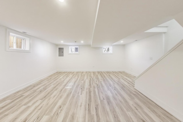 below grade area with electric panel, light wood-type flooring, baseboards, and recessed lighting