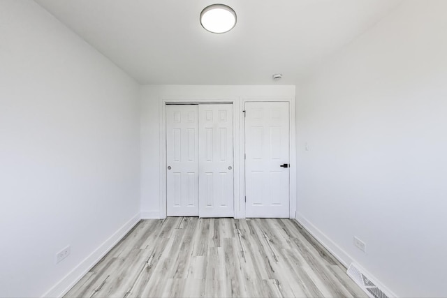 unfurnished bedroom with a closet, visible vents, light wood-style floors, and baseboards