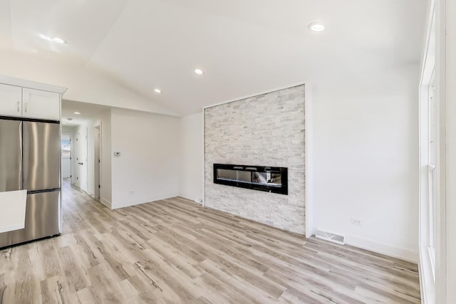 unfurnished living room with vaulted ceiling, a fireplace, visible vents, and light wood-type flooring