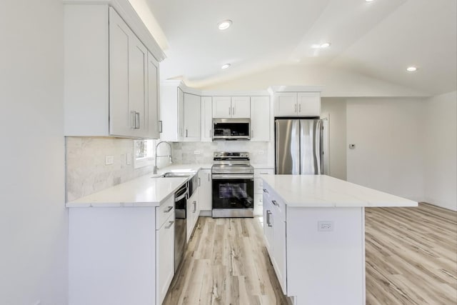 kitchen featuring light wood finished floors, a sink, vaulted ceiling, appliances with stainless steel finishes, and a center island