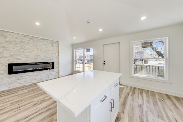 kitchen featuring light stone counters, light wood finished floors, a fireplace, vaulted ceiling, and white cabinetry