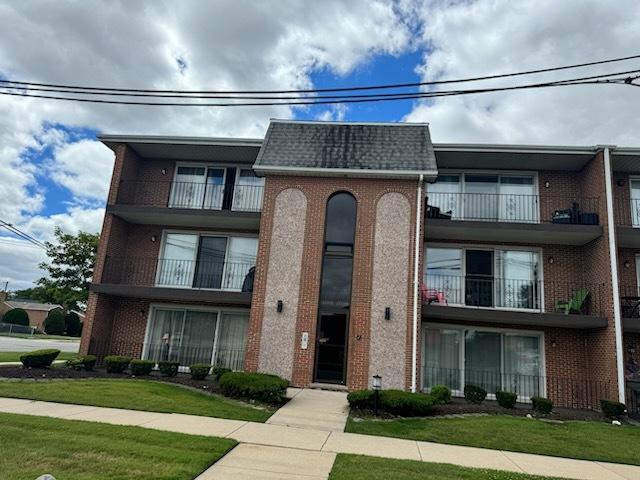 view of front of home featuring mansard roof, brick siding, a front lawn, and a shingled roof