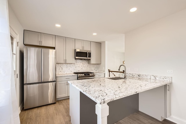 kitchen with gray cabinetry, stainless steel appliances, a peninsula, and a sink