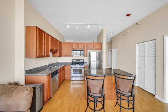 kitchen featuring dark stone countertops, light wood finished floors, a kitchen island, a sink, and appliances with stainless steel finishes