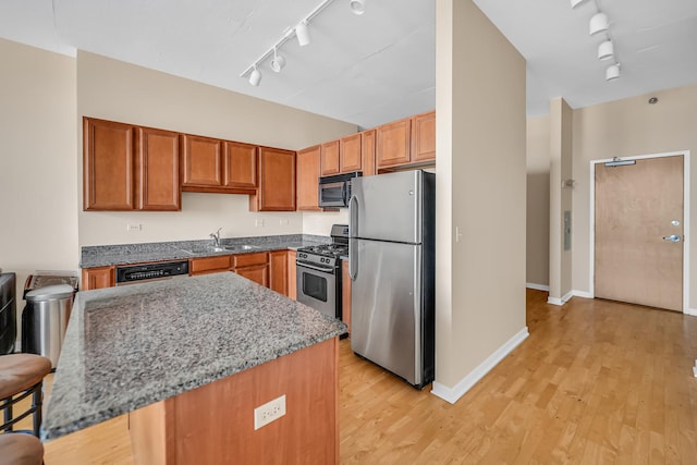 kitchen featuring a sink, appliances with stainless steel finishes, rail lighting, light wood finished floors, and light stone countertops