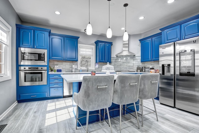 kitchen featuring blue cabinetry, appliances with stainless steel finishes, and wall chimney exhaust hood