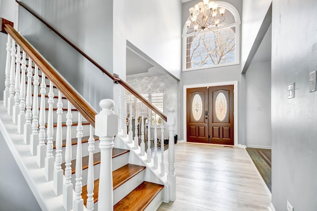 foyer entrance featuring wood finished floors, baseboards, stairs, a towering ceiling, and a chandelier