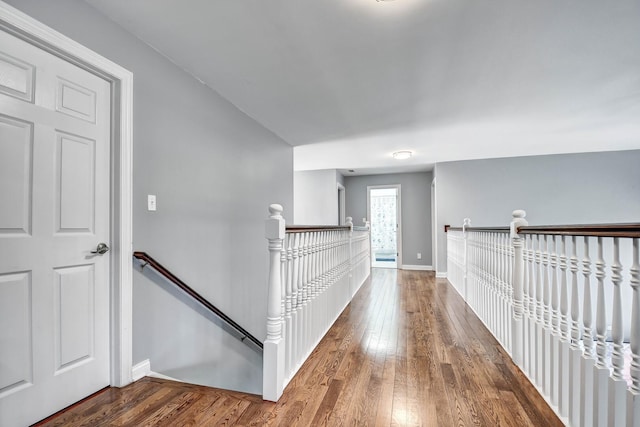 hall featuring an upstairs landing, baseboards, and hardwood / wood-style flooring