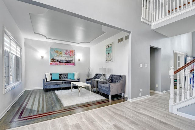 living room with wood finished floors, visible vents, baseboards, stairs, and a raised ceiling