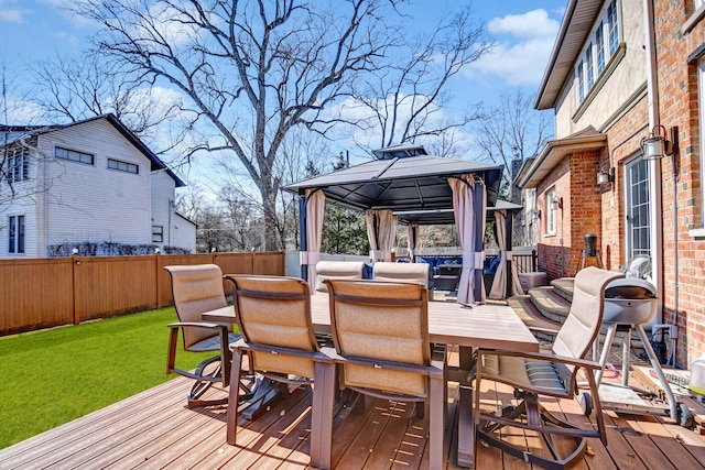 wooden terrace featuring a gazebo, a lawn, outdoor dining area, and fence