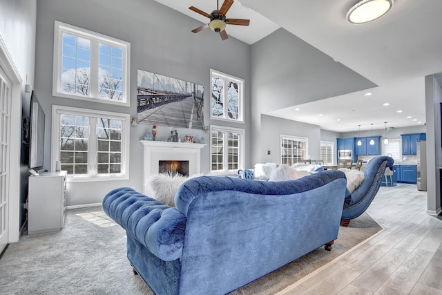 living room with baseboards, a lit fireplace, recessed lighting, light wood-style floors, and a towering ceiling