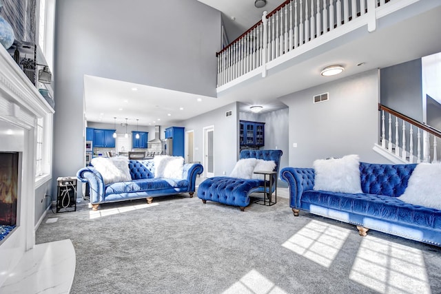 carpeted living area featuring visible vents, stairway, a high ceiling, and baseboards