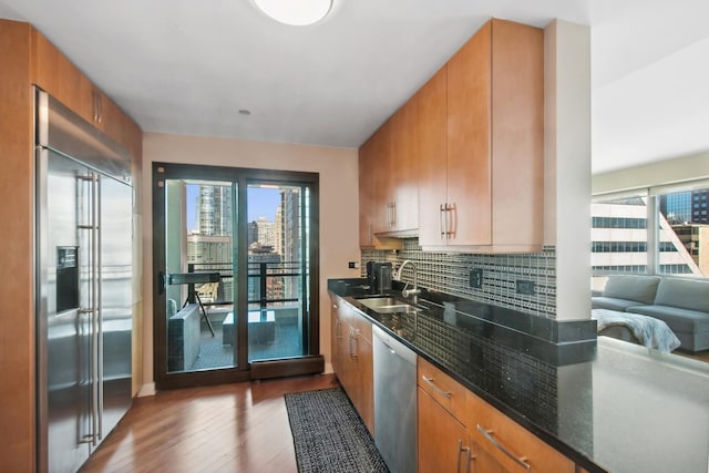 kitchen with a sink, backsplash, wood finished floors, stainless steel appliances, and dark stone counters