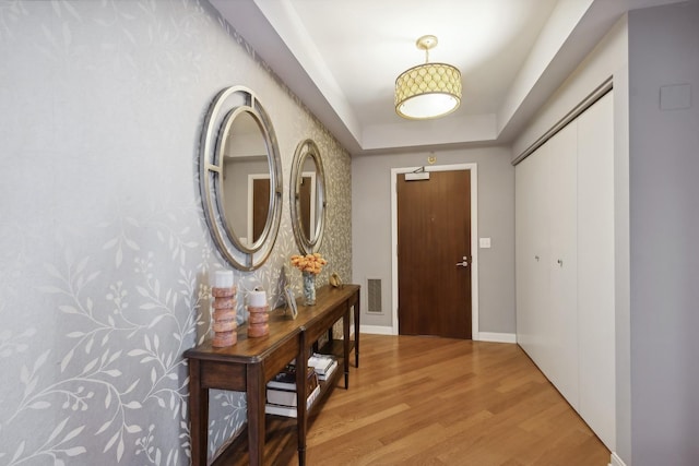 foyer with visible vents, baseboards, a tray ceiling, and wood finished floors