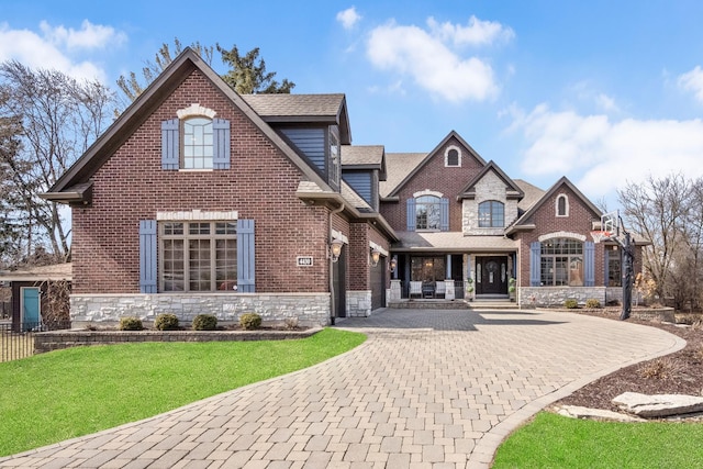 view of front facade featuring brick siding, a front yard, decorative driveway, a garage, and stone siding