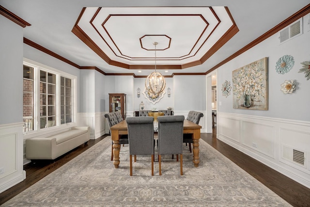 dining space with visible vents, a wainscoted wall, a notable chandelier, wood finished floors, and a raised ceiling