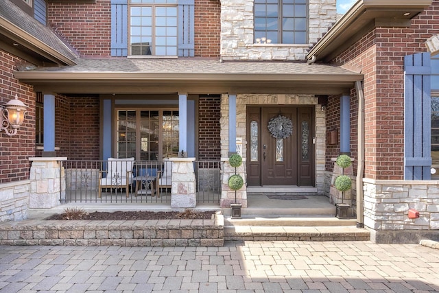 entrance to property featuring brick siding, a porch, and roof with shingles