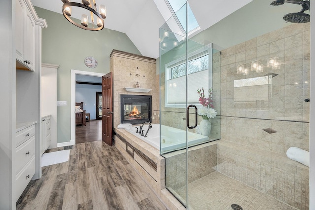 bathroom with a tiled fireplace, vaulted ceiling with skylight, a stall shower, wood finished floors, and ensuite bath