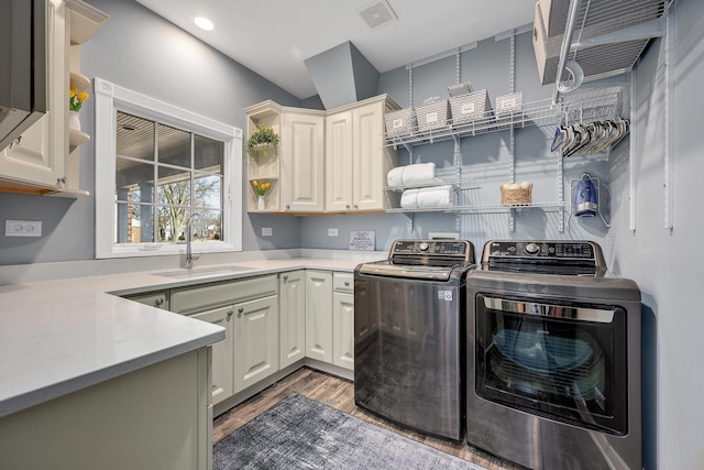 laundry area featuring washing machine and clothes dryer, visible vents, light wood finished floors, cabinet space, and a sink