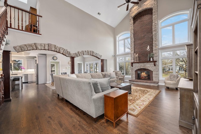 living room with high vaulted ceiling, dark wood finished floors, arched walkways, a fireplace, and ceiling fan