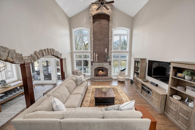 living room with light wood finished floors, a brick fireplace, high vaulted ceiling, and a ceiling fan