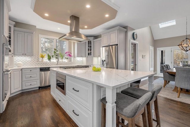 kitchen with light stone counters, a kitchen island, appliances with stainless steel finishes, island range hood, and glass insert cabinets