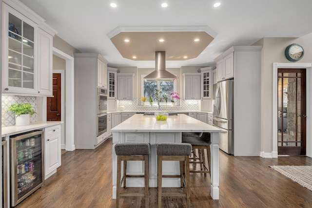 kitchen with a raised ceiling, beverage cooler, dark wood-type flooring, and appliances with stainless steel finishes