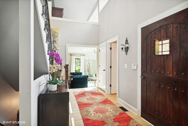 entryway featuring light tile patterned floors, visible vents, baseboards, and a high ceiling