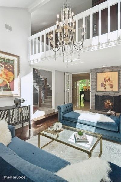 living area with visible vents, wood finished floors, stairway, a brick fireplace, and a towering ceiling