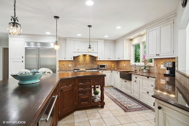 kitchen with a sink, dark countertops, pendant lighting, and built in fridge