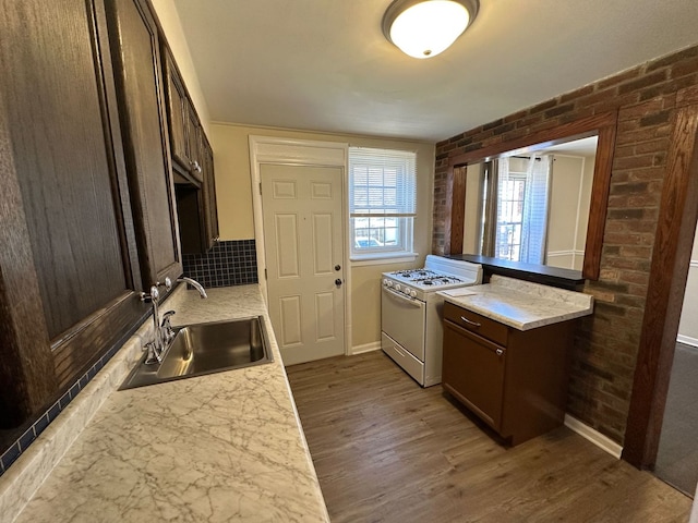 kitchen featuring brick wall, dark wood finished floors, white range with gas cooktop, a sink, and dark brown cabinets