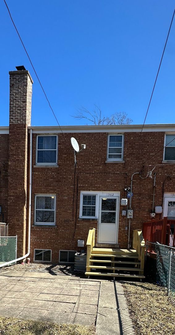 back of house with brick siding, entry steps, a chimney, and fence