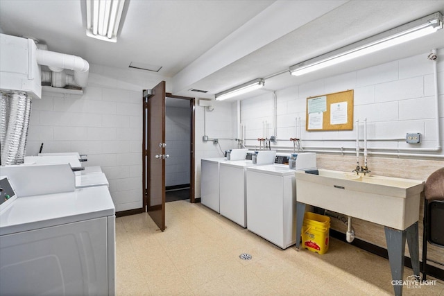 community laundry room with washer and dryer, concrete block wall, and light floors