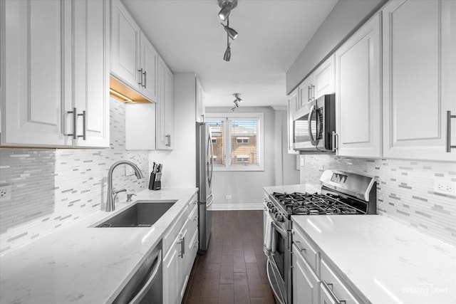 kitchen with light stone countertops, decorative backsplash, white cabinets, stainless steel appliances, and a sink