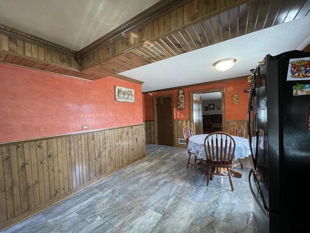 dining area featuring wooden walls, wainscoting, a textured ceiling, and ornamental molding