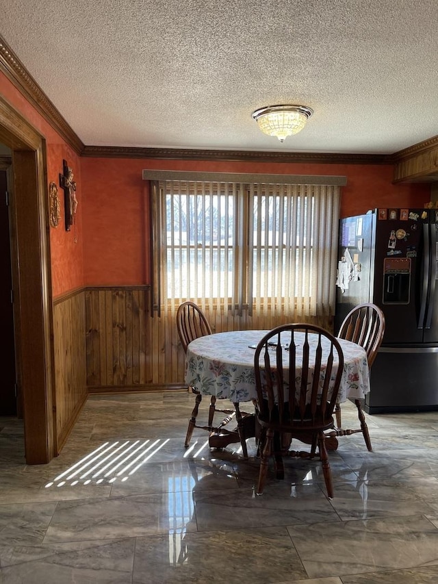 dining room with a textured ceiling, wooden walls, ornamental molding, and wainscoting