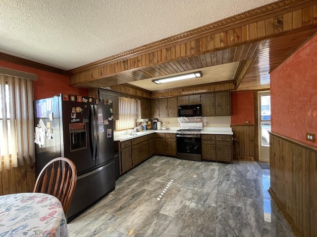 kitchen featuring a wainscoted wall, black appliances, a textured ceiling, wooden walls, and light countertops