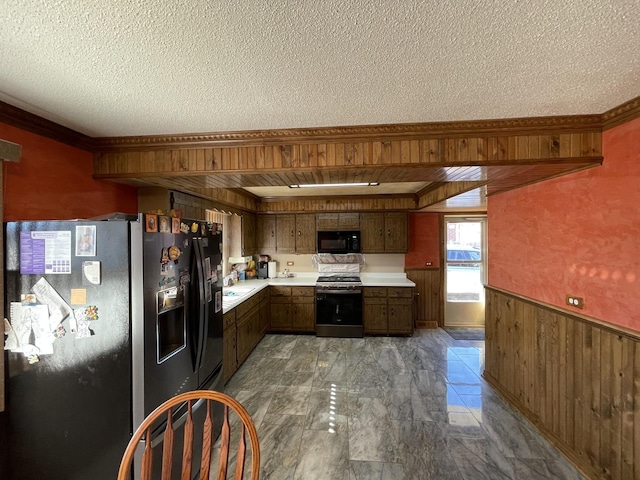 kitchen featuring black appliances, a textured ceiling, wooden walls, wainscoting, and light countertops